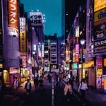 Explore the lively streets of Shinjuku, Tokyo at night with colorful lights and bustling activity.