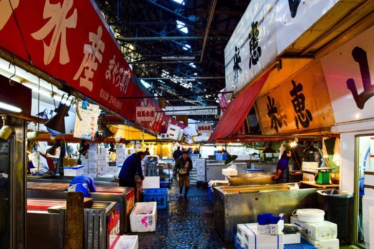 A vibrant scene of vendors and shoppers at Tsukiji fish market in Tokyo during nighttime.