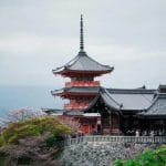 Kiyomizu-dera temple surrounded by lush greenery and cherry blossoms in Kyoto, Japan.